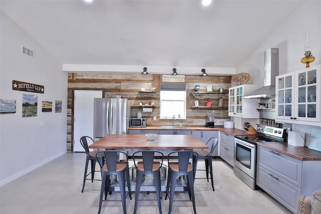 kitchen with stainless steel appliances, wall chimney exhaust hood, sink, a kitchen bar, and wood counters