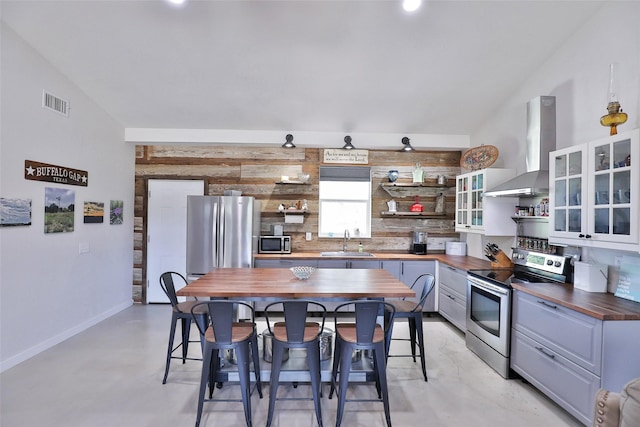 kitchen featuring a sink, wooden counters, wall chimney range hood, stainless steel appliances, and open shelves