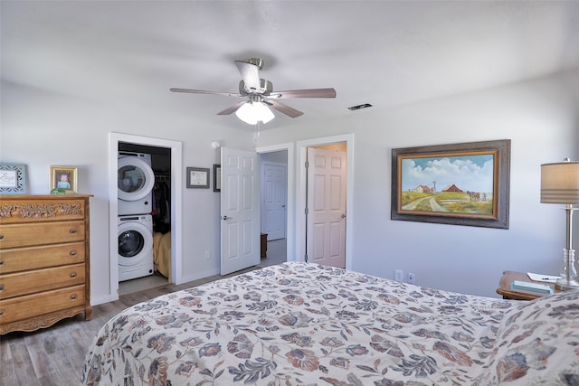 bedroom featuring wood-type flooring, stacked washer / drying machine, and ceiling fan