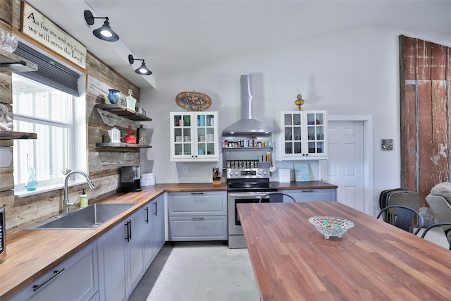 kitchen with electric range, sink, butcher block counters, and wall chimney range hood