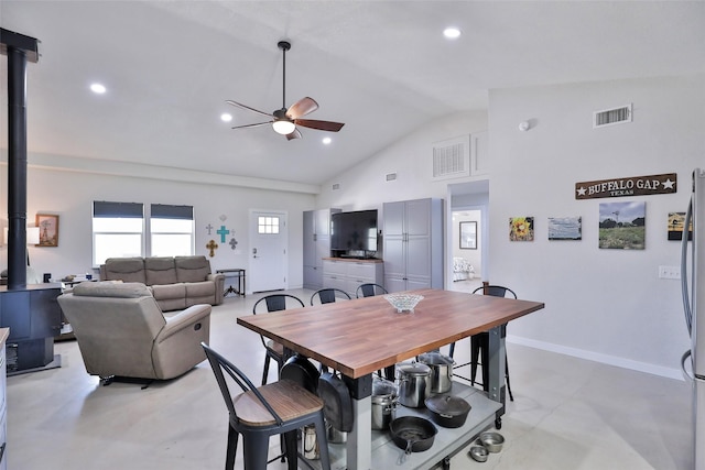 dining space featuring visible vents, baseboards, a wood stove, high vaulted ceiling, and a ceiling fan