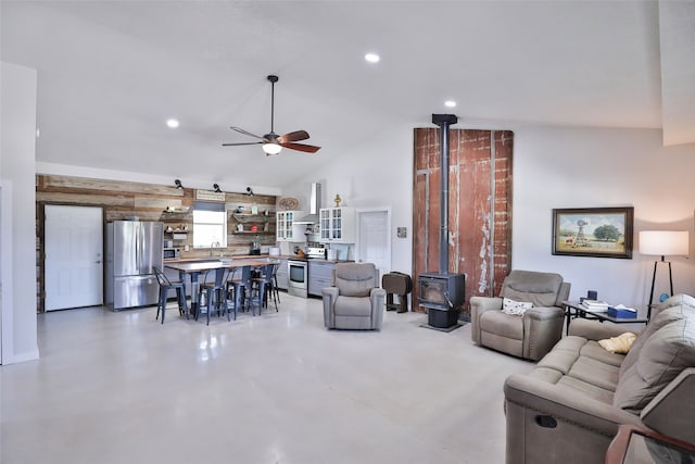 living room featuring ceiling fan, a wood stove, sink, vaulted ceiling, and concrete floors