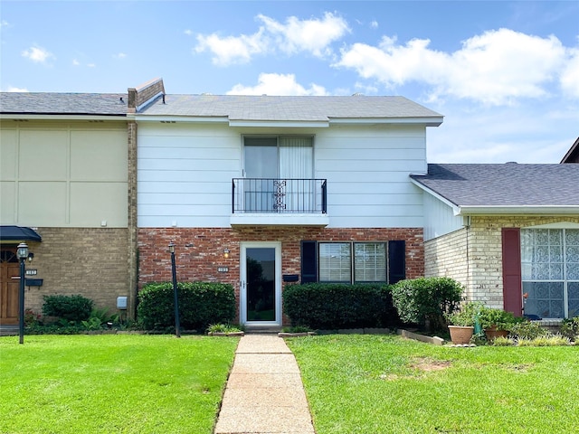 view of front of property with brick siding, a balcony, and a front lawn