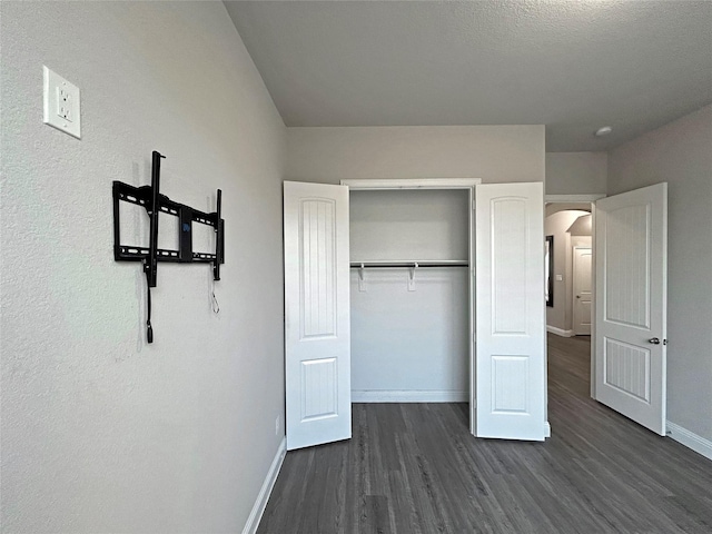 unfurnished bedroom featuring a textured ceiling, dark hardwood / wood-style flooring, and a closet