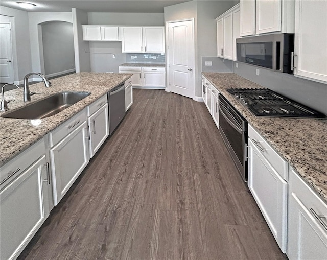 kitchen featuring dark wood-type flooring, sink, light stone countertops, appliances with stainless steel finishes, and white cabinetry