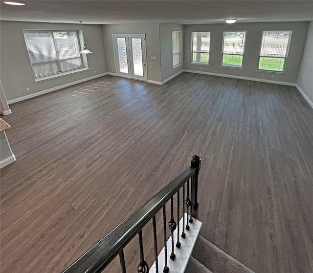 unfurnished living room with plenty of natural light, dark wood-type flooring, and french doors