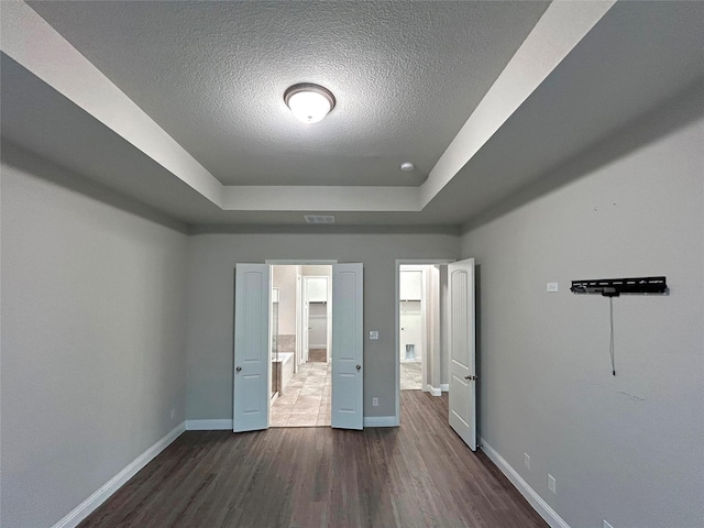 unfurnished bedroom featuring a textured ceiling, a tray ceiling, and dark wood-type flooring