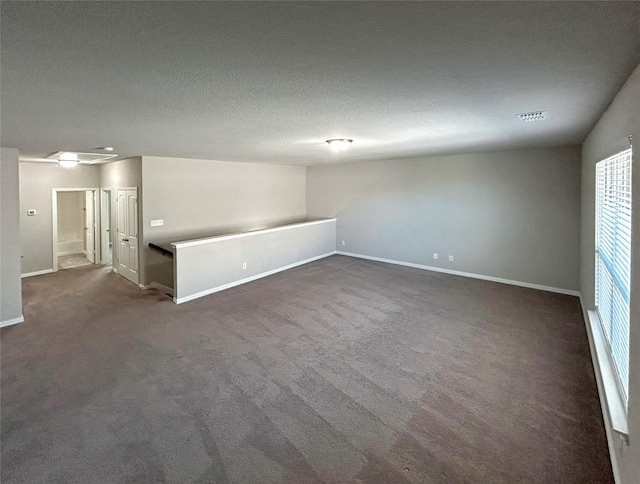 empty room with a textured ceiling and dark colored carpet