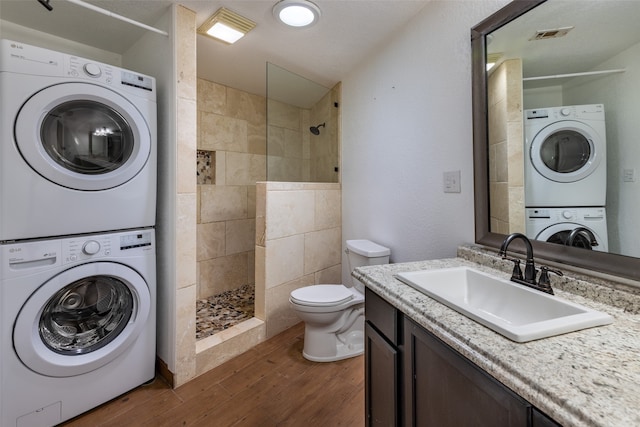 bathroom with tiled shower, hardwood / wood-style floors, stacked washer and clothes dryer, and sink