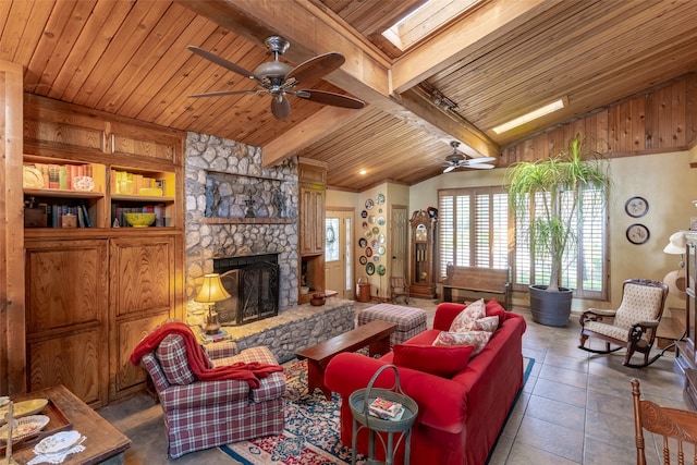 tiled living room with vaulted ceiling with skylight, ceiling fan, a stone fireplace, and wooden ceiling