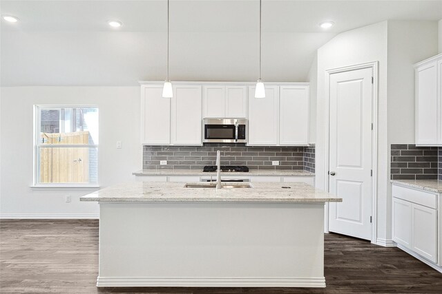 kitchen featuring decorative light fixtures, tasteful backsplash, white cabinetry, light stone counters, and a center island with sink