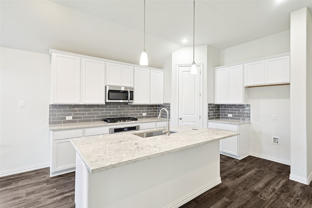 kitchen with appliances with stainless steel finishes, sink, white cabinetry, light stone counters, and a center island with sink