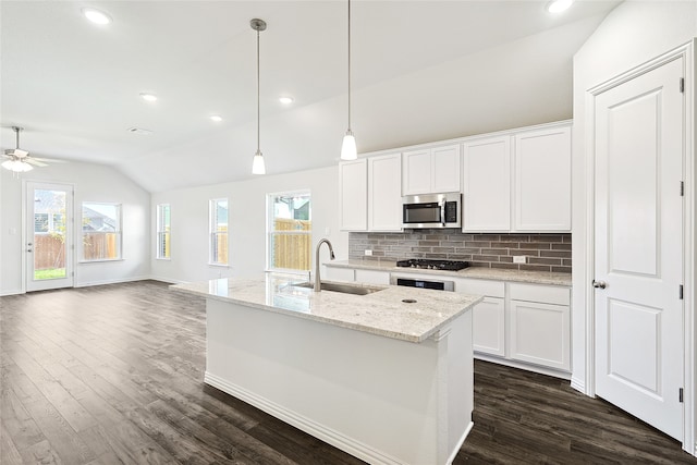 kitchen with light stone countertops, decorative light fixtures, white cabinetry, sink, and vaulted ceiling