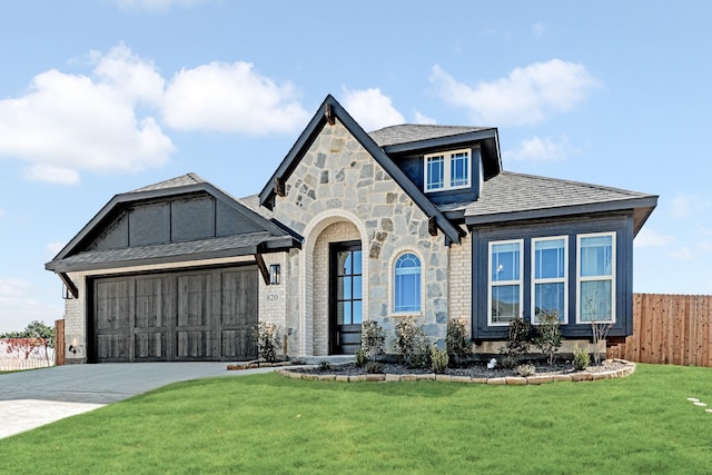 english style home featuring a garage, fence, driveway, stone siding, and a front yard