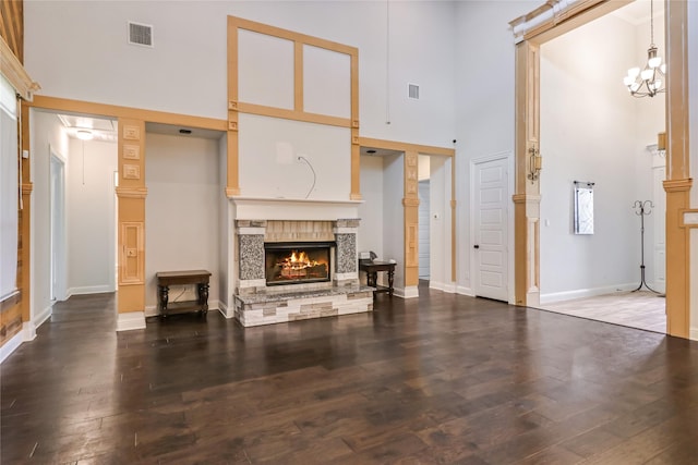 living room with hardwood / wood-style floors, a stone fireplace, a towering ceiling, and an inviting chandelier