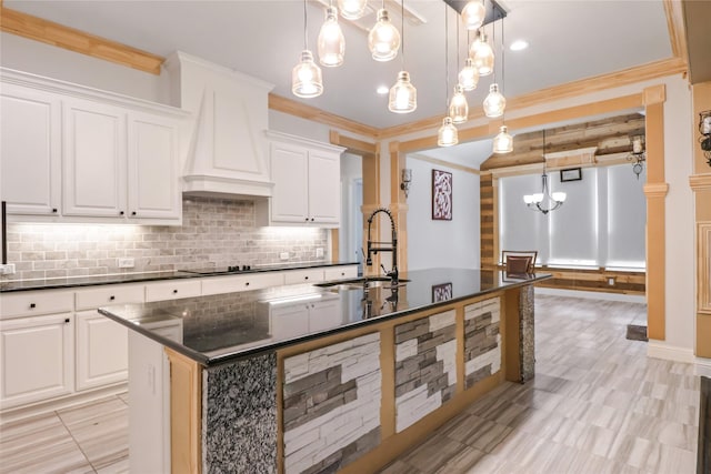 kitchen with custom exhaust hood, a kitchen island with sink, sink, white cabinetry, and hanging light fixtures