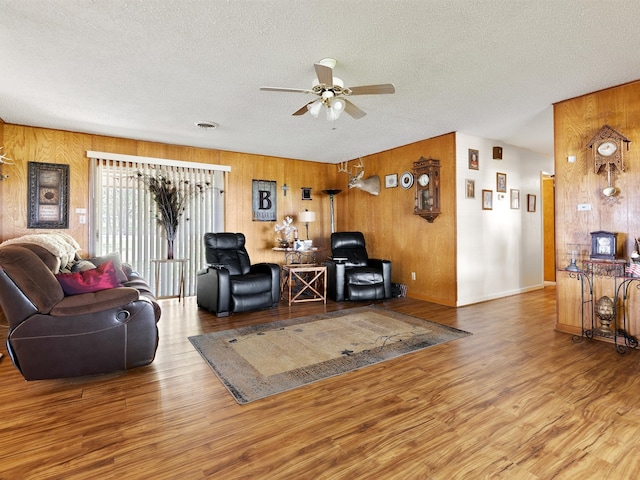 living room featuring ceiling fan, hardwood / wood-style flooring, wooden walls, and a textured ceiling