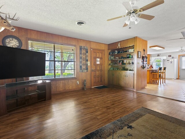 unfurnished living room featuring hardwood / wood-style flooring, a textured ceiling, wooden walls, and ceiling fan