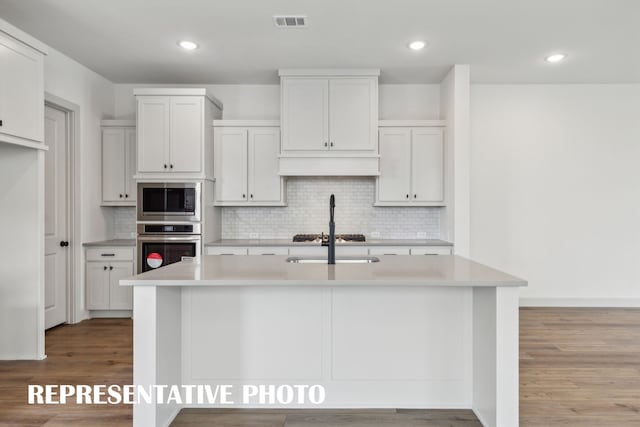 kitchen featuring stainless steel appliances, a center island with sink, white cabinets, and light hardwood / wood-style flooring