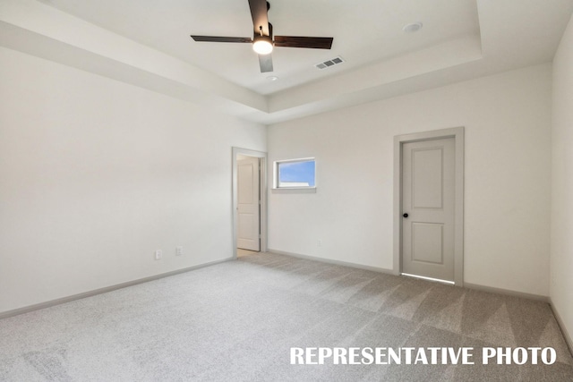 carpeted spare room with a raised ceiling and ceiling fan