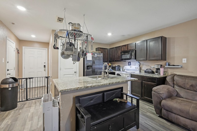 kitchen featuring stainless steel fridge, an island with sink, light wood-type flooring, dark brown cabinetry, and white range with electric cooktop