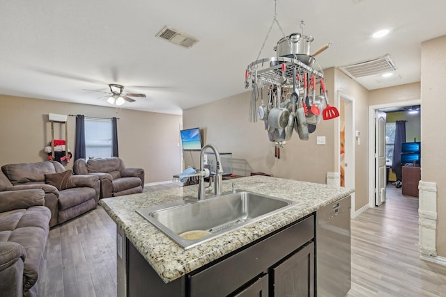 kitchen featuring dishwasher, sink, a kitchen island with sink, light wood-type flooring, and light stone counters