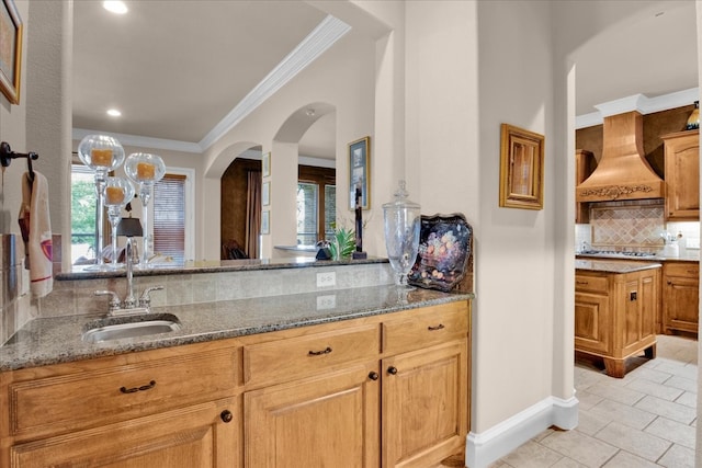 kitchen with backsplash, custom range hood, light stone countertops, crown molding, and sink