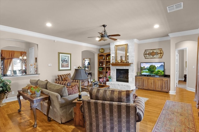 living room featuring ceiling fan with notable chandelier, crown molding, a stone fireplace, and light wood-type flooring