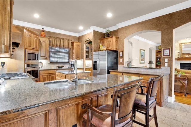 kitchen featuring kitchen peninsula, sink, appliances with stainless steel finishes, a stone fireplace, and a breakfast bar area