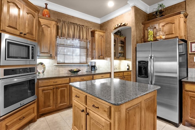 kitchen featuring appliances with stainless steel finishes, a kitchen island, dark stone counters, ornamental molding, and light tile patterned floors