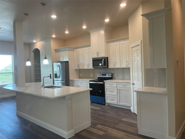 kitchen with white cabinetry, appliances with stainless steel finishes, a kitchen island with sink, and decorative light fixtures