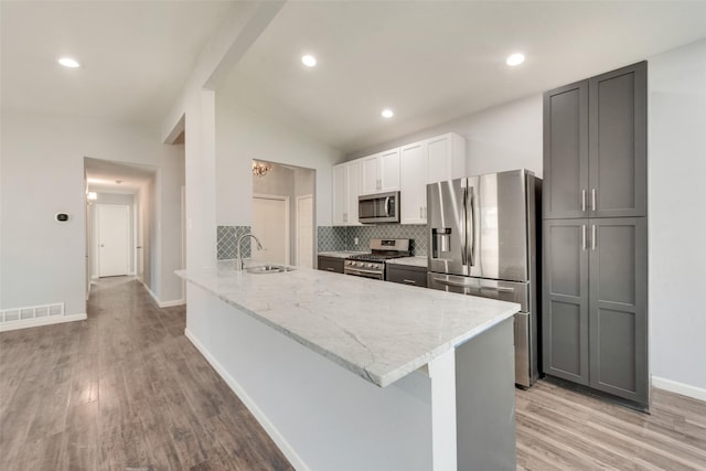 kitchen with a sink, appliances with stainless steel finishes, light wood-type flooring, light stone countertops, and tasteful backsplash