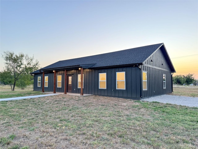 modern farmhouse style home featuring gravel driveway, a front lawn, board and batten siding, and a shingled roof