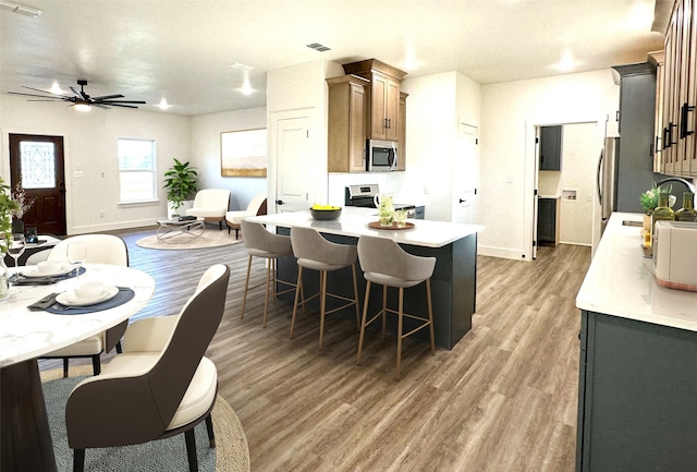 kitchen with a breakfast bar area, appliances with stainless steel finishes, ceiling fan, dark hardwood / wood-style flooring, and sink