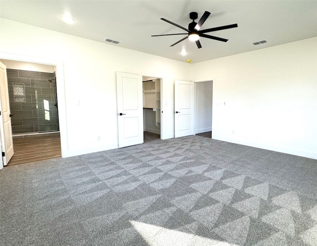 unfurnished bedroom featuring a closet, ensuite bath, dark colored carpet, ceiling fan, and a spacious closet