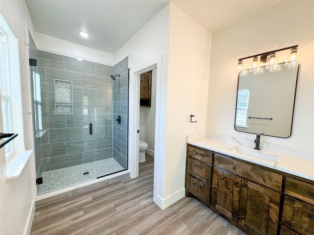 bathroom with a shower with door, hardwood / wood-style floors, vanity, and toilet