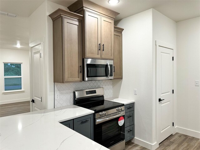 kitchen featuring stainless steel appliances, light hardwood / wood-style floors, tasteful backsplash, and light stone countertops