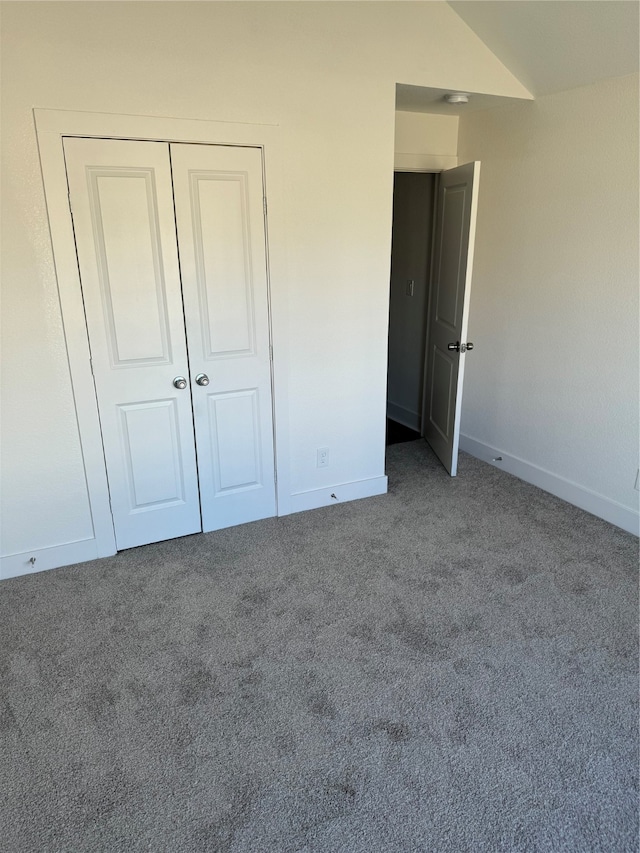 unfurnished bedroom with a closet, lofted ceiling, and dark carpet