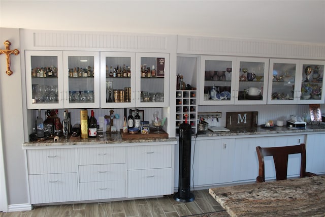 bar featuring white cabinets, hardwood / wood-style flooring, and dark stone counters