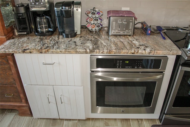 kitchen featuring white cabinets, light stone counters, and stainless steel oven