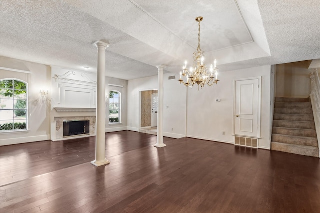 unfurnished living room with a raised ceiling, dark hardwood / wood-style flooring, a wealth of natural light, and an inviting chandelier