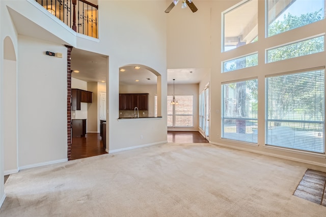 unfurnished living room with a towering ceiling, ceiling fan with notable chandelier, carpet floors, and a wealth of natural light