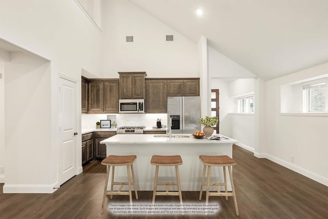 kitchen featuring a center island with sink, stainless steel appliances, high vaulted ceiling, and a breakfast bar area