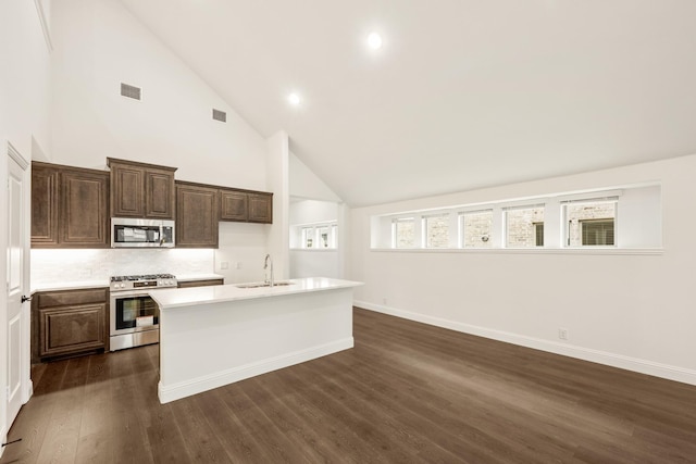 kitchen with appliances with stainless steel finishes, backsplash, sink, a center island with sink, and high vaulted ceiling