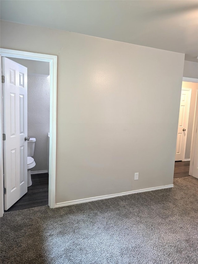 unfurnished bedroom featuring dark carpet and ensuite bathroom