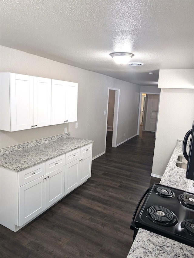 kitchen with a textured ceiling, light stone countertops, white cabinets, and black / electric stove