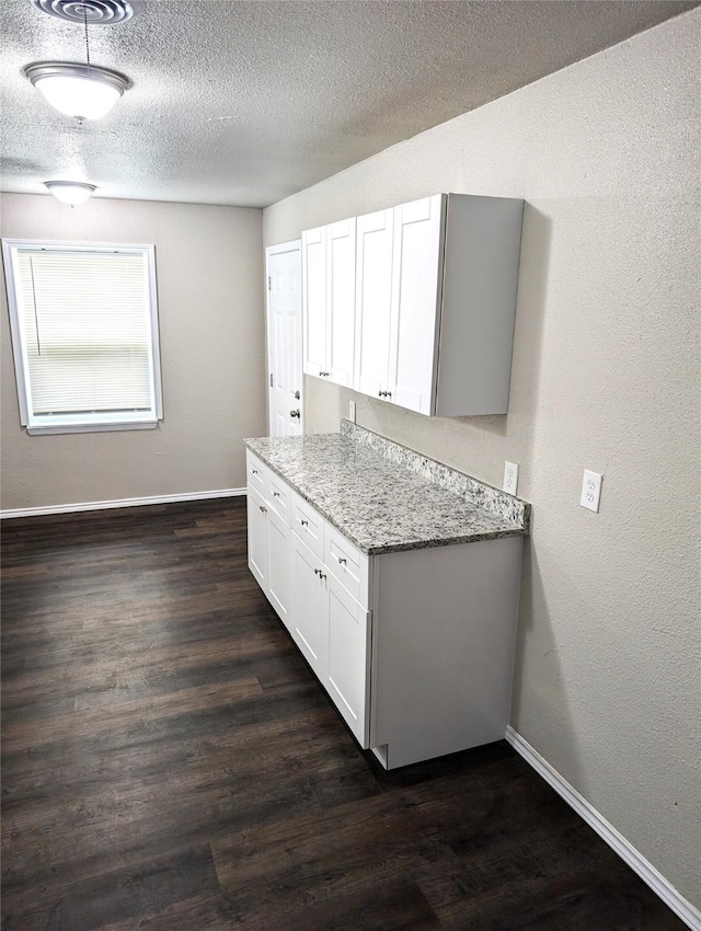 kitchen featuring light stone countertops, a textured ceiling, white cabinets, and dark hardwood / wood-style floors