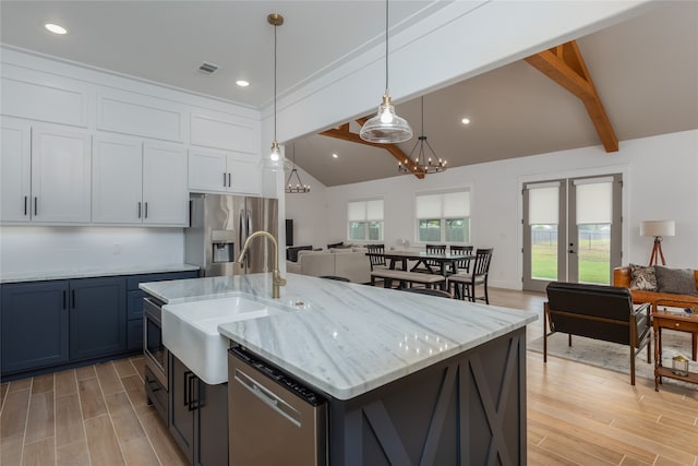 kitchen with a center island with sink, light wood-type flooring, vaulted ceiling with beams, stainless steel appliances, and sink