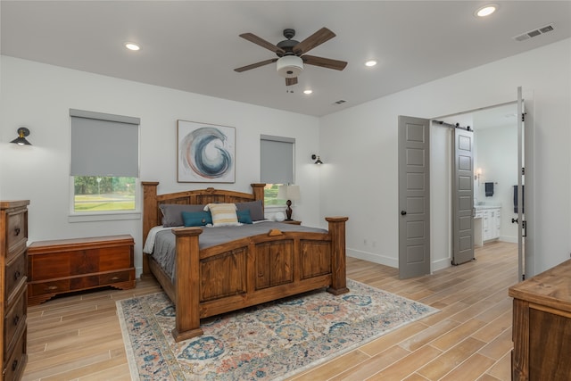 bedroom with ceiling fan, multiple windows, light wood-type flooring, and a barn door