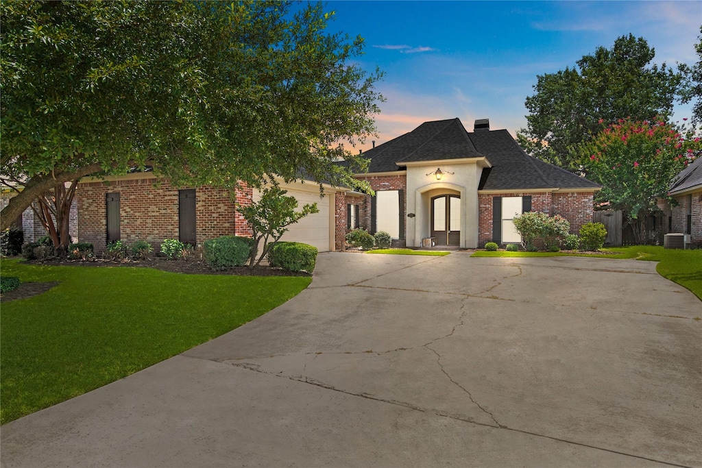 french country inspired facade featuring cooling unit, a garage, and a lawn